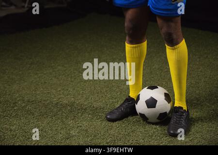 Athlète masculin debout sur gazon attrapant un ballon de football dans des chaussettes jaunes, un short bleu et des crampons noirs Banque D'Images