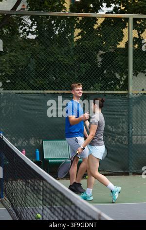 Un couple profite d'une partie de tennis amicale sur un court extérieur par une journée ensoleillée, partageant rires et excitation lors d'un après-midi de plaisir et de compétition Banque D'Images