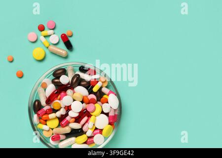 Assortiment de pilules et capsules pharmaceutiques colorées dans un bol en verre sur un fond vert menthe, santé et médecine Banque D'Images