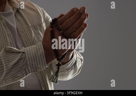 Mains de personnes âgées jointes en prière tenant un chapelet en bois avec une croix et une pampille, dévotion spirituelle et foi, les grains du chapelet sont un symbole de Banque D'Images