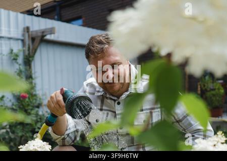 Jeune jardinier arrosant des arbustes d'hortensia blancs pendant l'été pour maintenir les plantes ornementales saines et florissantes dans un jardin domestique. Banque D'Images
