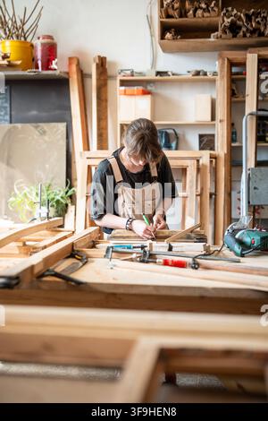 Femme charpentier concentrée travaillant dans un atelier de menuiserie sur la restauration d'un cadre de fenêtre en bois antique. Banque D'Images