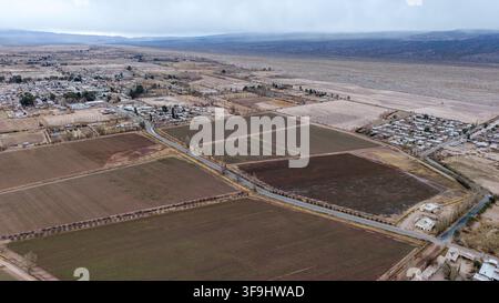 Vue aérienne de champs agricoles et d'une route menant à la ville, dans un vaste paysage aride à Barreal, province de San Juan, en Argentine. Banque D'Images