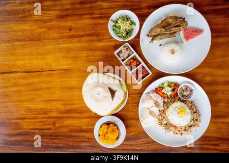 Festin balinais avec Bebek Goreng, Nasi Goreng, noix de coco fraîche et sambal sur un fond en bois rustique avec espace libre Banque D'Images
