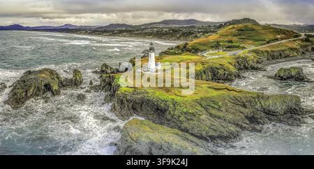 Vue aérienne du phare de Yaquina Head sur une pointe rocheuse entourée de l'océan Pacifique avec une végétation côtière sous un ciel nuageux à Newport, Oreg Banque D'Images