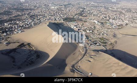 Vue aérienne de l'oasis de Huacachina entourée d'immenses dunes de sable et de la ville d'Ica, Ica, Pérou. Banque D'Images