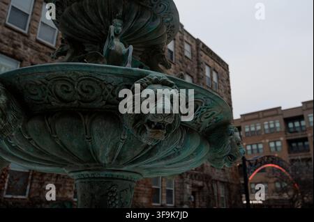 Des têtes de lion patinées et des motifs de rinceaux ornent une fontaine en bronze ornée devant une architecture en pierre Banque D'Images