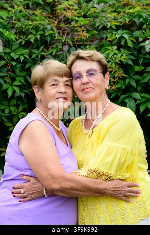 Deux sœurs russes âgées heureuses s'embrassant et montrant de l'amour près d'un mur de lierre vert dans un jardin rural. Banque D'Images