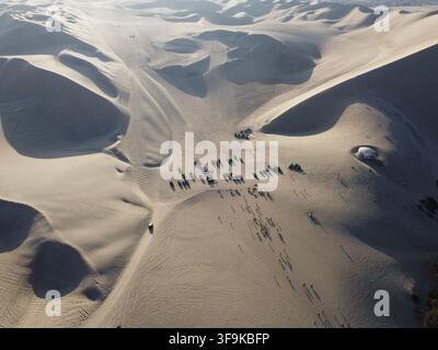 Vue aérienne des dunes de sable de Huacachina avec des buggies de sable garés et des personnes marchant à travers le vaste paysage désertique d'Ica, Ica, Pérou Banque D'Images