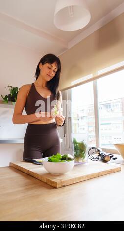 Femme en tenue de sport préparant une salade verte fraîche pour un smoothie sain dans sa cuisine Banque D'Images