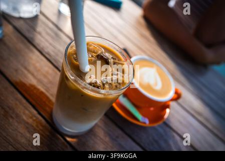 Latte glacé avec une paille et du café chaud dans une tasse sur une table en bois Banque D'Images