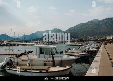 Bar, Monténégro – 26 juin 2026. Des bateaux à moteur s'alignent le long d'une jetée de marina avec une eau calme, des bâtiments de ville côtière et des montagnes escarpées qui s'élèvent en arrière-plan. Banque D'Images