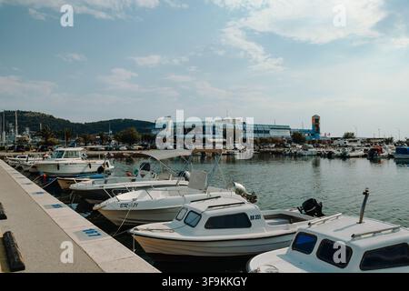 Bar, Monténégro – 26 juin 2026. Des bateaux à moteur s'alignent le long d'une jetée de marina avec une eau calme, des bâtiments de ville côtière et des montagnes escarpées qui s'élèvent en arrière-plan. Banque D'Images