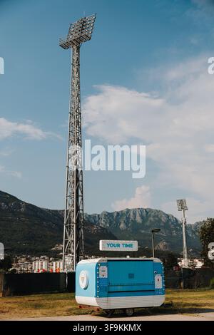 Bar, Monténégro - 26 juin 2026. De hautes tours de projecteurs de stade s'élèvent au-dessus d'un petit kiosque avec des montagnes escarpées et un ciel bleu en arrière-plan. Banque D'Images