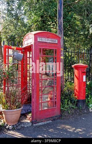 Une cabine téléphonique rouge K6 vintage réaménagée avec un cache-pot à côté d'une boîte aux lettres rouge iconique sur un bord de route ensoleillé à Caversham, Reading, Royaume-Uni, capturée Banque D'Images