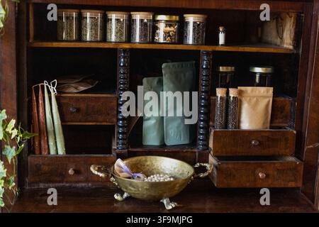 Armoire apothicaire vintage en bois avec des bocaux en verre pour épices, des herbes séchées, des sachets d'emballage, des bougies coniques et un bol en laiton à pieds avec des perles. Banque D'Images