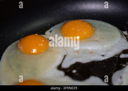 Deux œufs au plat frits dans une poêle noire avec des jaunes vifs orange et des blancs fermes. Nourriture pour le petit-déjeuner, cuisine maison, nutrition simple, repas protéiné, fraisne Banque D'Images