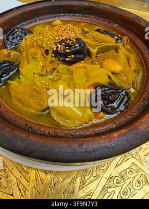 Tajine marocaine traditionnelle avec agneau tendre, prunes et graines de sésame grillées dans un plat en terre cuite. Banque D'Images