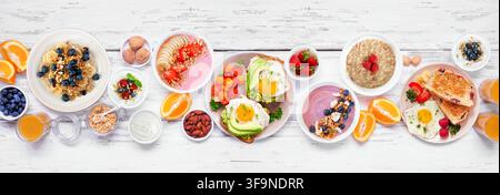 Scène de petit-déjeuner ou brunch sain sur un fond de bannière en bois blanc. Vue aérienne. Toast à l'avocat, bols de smoothies, avoine, yaourt et une variété de Banque D'Images