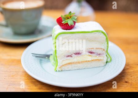 Tranche de gâteau princesse suédois traditionnel avec du marzipan vert, de la crème fouettée, une génoise et une garniture aux fruits rouges, recouvert d'une fraise fraîche et servi avec c Banque D'Images