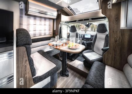 Vue de l'intérieur d'un camping-car moderne avec une table à manger dressée pour un repas, des sièges confortables et des armoires en bois, une paysage enneigé visible à travers Banque D'Images