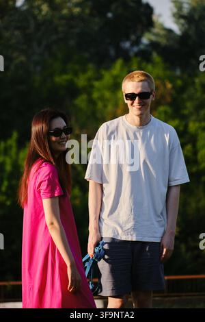 Jeune couple souriant portant des lunettes de soleil debout ensemble sur l'herbe dans le parc. Style de vie estival en extérieur. Banque D'Images