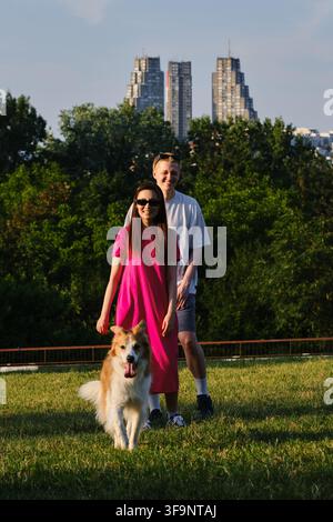 Chien courant sur l'herbe avec un couple heureux qui s'embrasse en arrière-plan. Animaux de compagnie, amour et style de vie en plein air. Banque D'Images