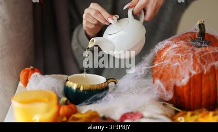 Composition automnale. Les mains de la femme versent le thé devant la fenêtre avec des feuilles d'automne Banque D'Images