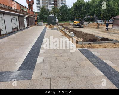 Chantier urbain montrant des travaux de rénovation de trottoir en cours. Des pavés gris clair nouvellement posés avec des bandes d'accentuation gris foncé courent en parallèle Banque D'Images