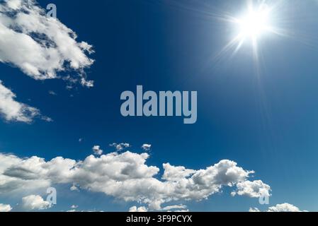 Journée ensoleillée et lumineuse avec un ciel bleu vif rempli de nuages cumulus blancs et duveteux. Le soleil radieux brille magnifiquement dans le coin supérieur, projetant Banque D'Images