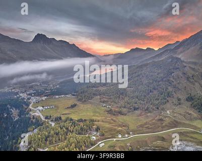 Vue aérienne de la vallée de l'Engadine avec une route sinueuse, des forêts luxuriantes et un lac serein sous un ciel dramatique au coucher du soleil avec des nuages bas dans les Grisons, Suisse Banque D'Images