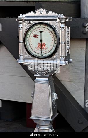 Balance vintage en argent se dresse contre un mur en bois. Le cadran semblable à une horloge affiche le prix '25c'. Travail métallique orné au design classique. Parfait pour rétro, vintage, Banque D'Images