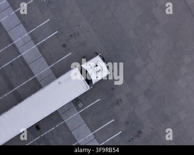 Vue aérienne d'un semi-remorque blanc garé dans un grand parking vide avec des lignes peintes en blanc à Gdańsk, en Pologne. Banque D'Images