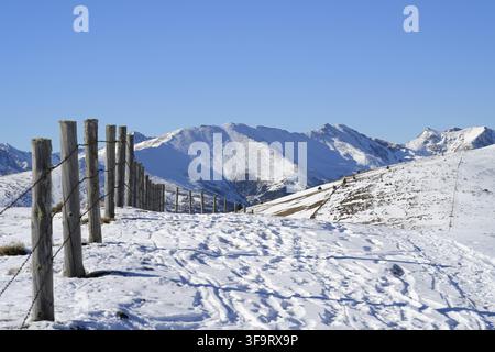 Panorama d'un paysage montagneux enneigé avec une clôture en bois à côté d'un sentier pour les skieurs de randonnée par une journée d'hiver claire Banque D'Images