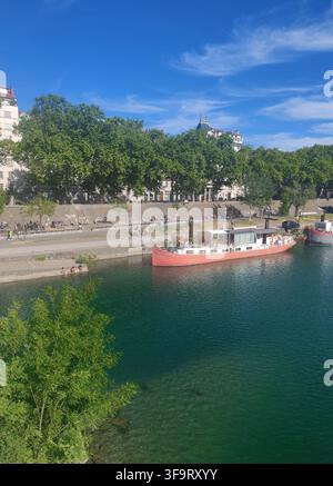 Lyon, France – 14 juin 2026 : Péniche naviguant sur le Rhône, vue d'un pont avec une eau bleu cristallin et un horizon urbain Banque D'Images