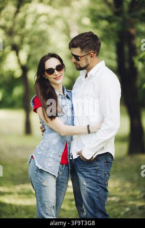 Portrait of young couple heureux en amour, souriant et embrassant dans le jardin. Les amateurs de sucré en portant des lunettes élégantes et des vêtements décontractés, posant un Banque D'Images