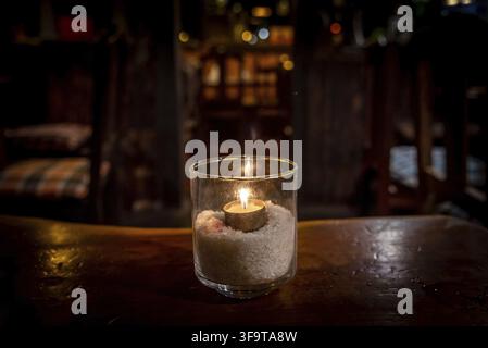 Feu isolé à l'intérieur d'un verre illuminant une scène sombre et des réflexions sur une table en bois et un arrière-plan bokeh agréable Banque D'Images