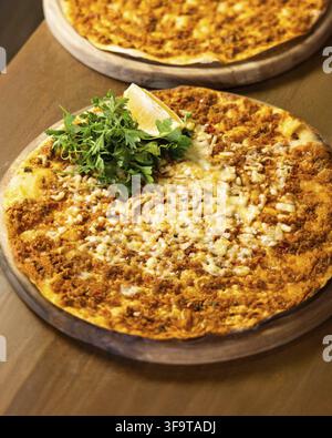 Vue rapprochée de deux lahmacuns traditionnels turcs servis sur des planches en bois, l'un avec du fromage fondu et une tranche de citron Banque D'Images