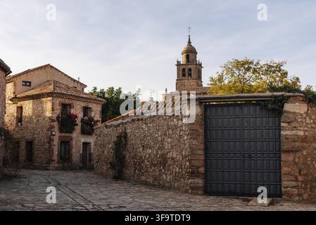 Rue du village de Medinaceli avec des maisons traditionnelles en pierre, un grand mur de pierre, une porte métallique et un clocher baroque Banque D'Images