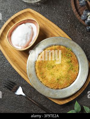 Dessert turc traditionnel Kunefe avec crème et pistaches, servi sur un plateau en bois Banque D'Images