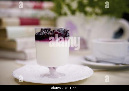 Dessert aux myrtilles avec du thé sur la table avec des fleurs et des livres Banque D'Images