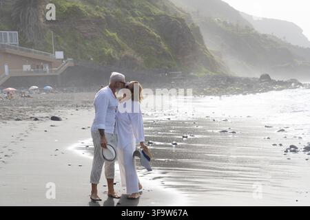 style de vie avec un couple de personnes âgées caucasiennes se reposant sur la plage, tenant les mains, heureux dans l'amour romantique et temps de détente, le tourisme de personnes âgées de famille, leis Banque D'Images
