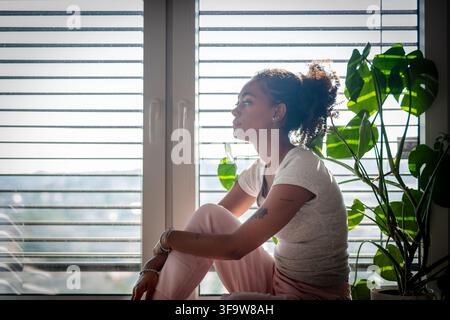 Femme se détendant près de la fenêtre et regardant dehors. Banque D'Images