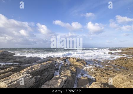 De puissantes vagues de l'Atlantique s'écrasent contre des falaises rocheuses le long de la côte de Bretagne en France. Sous un ciel bleu éclatant d'été, la mer étincelante et les côtes abruptes Banque D'Images