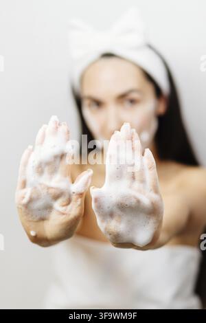 Femme appliquant une mousse faciale sur son visage, femme appliquant un nettoyant pour le visage. Jeune femme adulte utilisant un nettoyant moussant pour le nettoyage de la peau du visage Banque D'Images