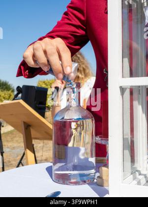 Personne en veste rouge retirant le bouchon d'une grande bouteille en verre remplie d'eau à l'extérieur Banque D'Images