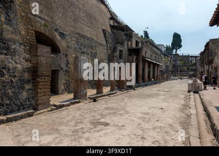 Vue le long du large Decumanus Maximus, bordé de portiques, de boutiques et de ruines de maçonnerie romaines, dans le parc archéologique d’Herculaneum, en Italie. Banque D'Images