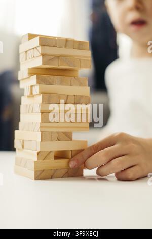 Gros plan sur les mains d'un garçon, en T-shirt blanc, jouant à la maison, sur la table à Jenga. Jeux de société pour enfants et adultes. Un passe-temps sans gadgets. Jeux d Banque D'Images