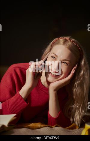 Image verticale d'une jeune femme caucasienne heureuse souriant tout en parlant au téléphone portable. L'image représente la communication mobile et convient aux campagnes publicitaires de télécommunication Banque D'Images