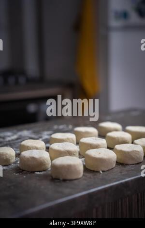 Portions de pâte de fromage frais de forme ronde disposées sur une table de cuisine farinée, préparant un petit-déjeuner traditionnel d'Europe de l'Est syrniki avant Banque D'Images